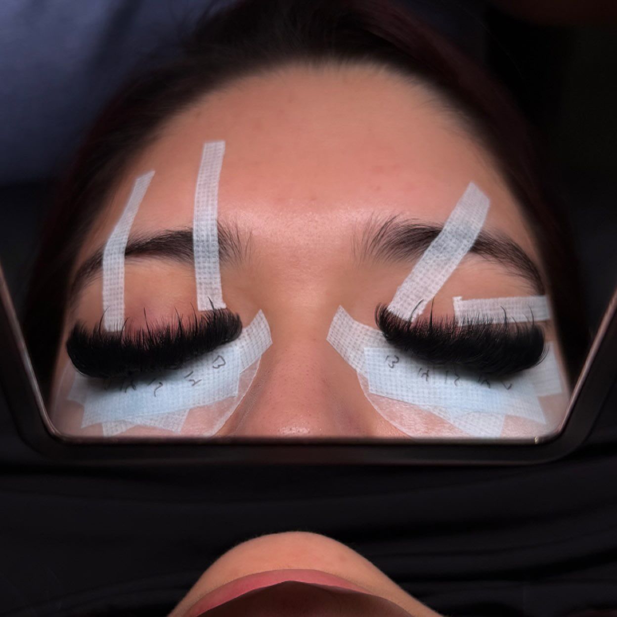 Lashes mapped and taped mid-appointment, seen in a mirror